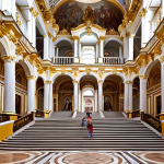 **

"Grand interior view of the Winter Palace's Jordan Staircase, showcasing its elaborate frescoes, statues, and gilded stucco. Capture the architectural masterpiece with tourists taking photos, emphasizing the scale and beauty."

**